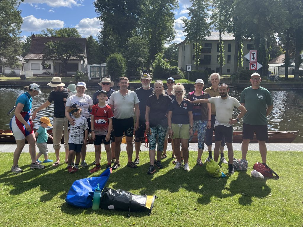 Eine Gruppe von Erwachsenen und Kindern posiert vor einem Gig-Vierer am Bootssteg