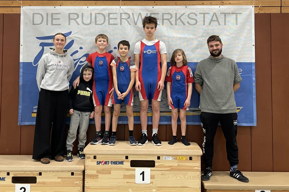 Fünf Kinder stehen auf einer Siegertribüne zwischen zwei jungen Erwachsenen
