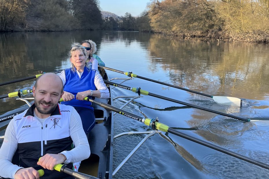 Vier Menschen im Gig-Vierer, im Hintergrund sonnenbeschienene Bäume