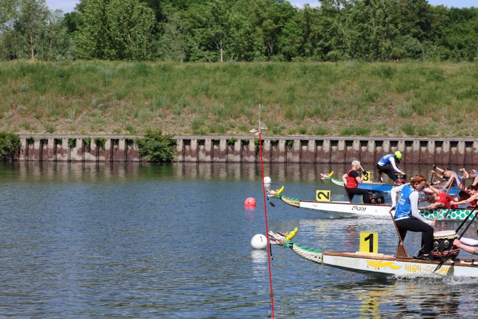 Von drei Drachenbooten ist jeweils nur der Bug und ein kleiner Teil des Paddelteams zu sehen. Zwei Boote liegen mit der Nase fast gleich nah an der Ziellinie