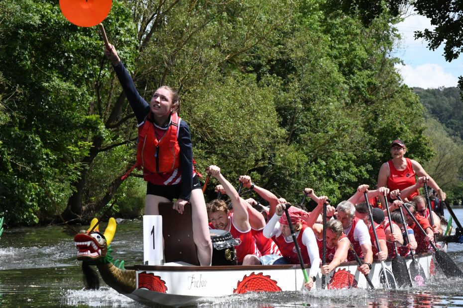 Ein vollbesetztes Drachenboot im Endspurt. Die Trommlerin schlägt an den Gong über der Ziellinie.