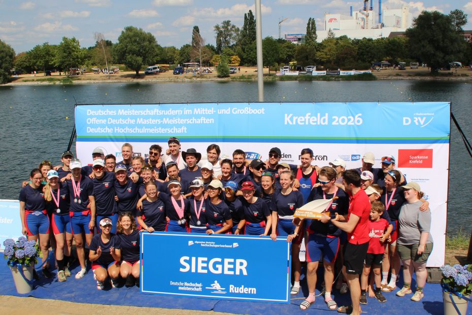 Eine Gruppe von Menschen im Ruderdress hat sich hinter einem Schild mit der Aufschrift "Sieger" versammelt